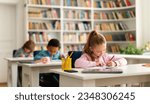 Small photo of Group of diverse schoolboys and schoolgirl sitting at desks in classroom at primary school, writing or drawing in notebook. Reopening and return back to school