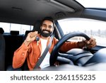Own Automobile. Proud Car Owner Indian Man Showing His New Auto Key Driving Vehicle, Sitting In Driver Seat With Hands On Steering Wheel, Smiling To Camera. Dreams Come True