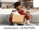 Small photo of Happy excited indian man unboxing parcel with new shoes at home, smiling eastern male opening cardboard box and looking at pair of white sneakers, satisfied with online shopping, free space