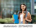 Small photo of Cheerful student clutching books at sunny campus. Happy young woman gripping books at vibrant campus, exuding positivity and youthful academic spirit, carrying backpack, copy space