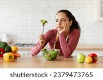 Small photo of Diet Struggles. Frustrated fit lady in activewear eating vegetable salad and looking at fork with upset expression, tired of diet menu and lack of appetite in modern kitchen at home