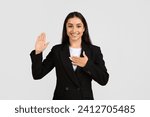 Small photo of Sincere european businesswoman making pledge or swearing an oath with her right hand raised and left hand on her chest on grey background