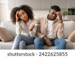 Small photo of Unwanted Pregnancy. Upset Child Free African American Couple Holding Positive Pregnancy Test, Feeling Stressed Sitting On Couch At Home. Unplanned Childbirth, Unintended Pregnancies Concept