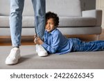 Small photo of Distressed black boy holding onto his father's leg tightly, showing plea for attention or refusal to let go, while the parent stands firm, home interior