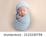Small photo of Newborn baby boy swaddled in blue fabric sleeping. Infant child kid resting during studio photoshoot