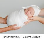 Small photo of Newborn baby sleeping in parents hands. Infant kid swaddled in fabric napping and mother and father care about child