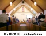 A blurred photo of the inside of a church sanctuary that is filled with people in the pews, and the pastor stands under a large cross at the altar.