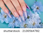 Hand with long artificial french manicured nails decorated with gemstones and blue flowers. Fashion and stylish manicure