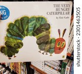 Small photo of Bangkok, Thailand - May 2023: “The Very Hungry Caterpillar” board book by Eric Carle in front of a book shelf in a book store