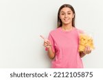 Small photo of Young Indian woman holding crips isolated on white background smiling and pointing aside, showing something at blank space.