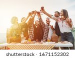 Group of friends making a toast during a barbecue in the countryside - Happy people having fun at a picnic on the hills in summer at sunset