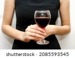 A woman holds a glass goblet with red wine in her hands, to celebrate the holiday. Close-up, soft focus.