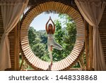 Woman practising yoga (tree pose) in bamboo house studio. View of nature and mountains on background. Peaceful meditation spot. Ecolodge retreat, eco friendly house