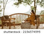 A girl is relaxing and drinking coffee on a balcony in a bamboo house overlooking the mountains. Coffee overlooking the mountains in Bali.
