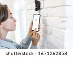 Woman controlling alarm system with smart phone and special mobile application wireless, standing near the motion sensor indoors