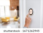 Woman regulating heating temperature with a modern wireless thermostat installed on the white wall at home. Cropped view focused on hand