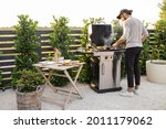 Small photo of Man cooking on the modern gas grill at beautiful backyard on a sunset. Cooking food on the open air