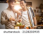 Small photo of Two guys of different ethnicity having fun while making salad together on kitchen. Concept of gay couples and everyday life at home . Caucasian and hispanic man cooking healthy food