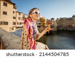 Young woman eating italian ice cream while sitting on the riverside with beautiful view on famous Old bridge in Florence at sunset. Concept of italian gastronomy and landmarks