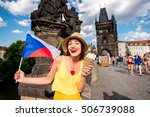 Young female tourist with traditional czech dessert called trdelnik and flag on Charles bridge in Prague