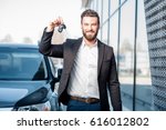 Happy buyer holding keys near the car in front of the modern avtosalon building
