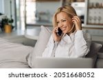 Businesswoman making a call while working on laptop on the bed