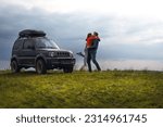 Happy couple kissing and hugging standing on the top of the mountain. Car trip on SUV with roof rack, trip at summer day. Man and woman enjoying time together travelling by vehicle. Ukraine
