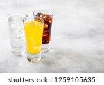 Glasses of soda drink with ice cubes and bubbles on stone kitchen background.