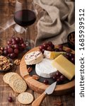Small photo of Glass of red wine with selection of various cheese on the board and grapes on wooden table background. Blue Stilton, Red Leicester and Brie Cheese and knife with linen kitchen cloth.