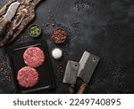 Sealed vacuum tray with two raw beef burgers with cleaver and barbeque fork and knife on black background. Top view