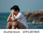 Small photo of Anxious depressed Asian man covering face with hands and bend down head