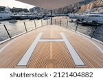The front deck of huge yacht in port of Monaco at sunset, the place for landing of helicopter, a lot of motorboats are on background, the chrome plated handrail, megayacht is moored in marina, dusk