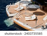 Small photo of Close-up view of a relaxation area on the open teak deck on the stern of an expensive huge mega yacht at sunny day, stairs to water, wealth life, lounge chairs