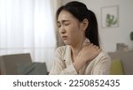 Small photo of asian female freelance worker having a sudden neck crick is massaging her stiff shoulders and relaxing her muscles while working at home in the living room