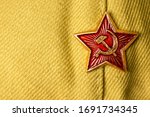 Small photo of Old soviet military badge with hammer and sickle on light green cloth headgear. Red five-pointed soviet communist gold red star. Symbol of the USSR. Space for the text. Victory Day Concept.