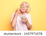 old woman applies an anti-aging facial mask with a finger.close up portrait. isolated yellow background. studio shot.beauty care, wellness, wellbeing.
