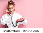 Agitated female with red hair in bathrobe and curlers talking on landline phone, retro srtyle. isolated over pink background. After shower, have conversation. People, fashion concept
