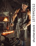 Small photo of caucasian young man forger having muscular body beat iron with hammer isolated in dark whorkshop. power and strength