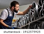 Small photo of bearded male auto mechanic in uniform is checking car discs represented for sale in service, examining, keep tabs on merchandise