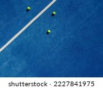 Overhead aerial view of three balls near the net of a blue paddle tennis court, sports courts