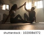 Healthy man and woman sitting on floor and giving each other high five at the gym. Fitness people after successful exercising session in gym.