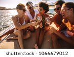 Multiracial group of people toasting drinks on the yacht deck and laughing. Cheerful men and woman partying on a boat.