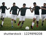 Small photo of Men playing soccer running after a football on a rainy morning. Footballers trying to take possession of the ball running on the field playing soccer.