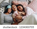 Small photo of Young girls lying on bed during a sleepover laughing while looking at mobile phone. Girl taking selfie using mobile phone lying on bed with friends at a sleepover.