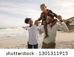 Parents carrying son on shoulders on beach vacation. African family of mother and father carrying son on his shoulders on vacation.