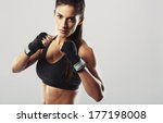 Pretty young woman wearing boxing gloves posing in combat stance looking at camera. Fit young female boxer ready for fight on grey background