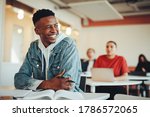 Small photo of Male student sitting in university classroom looking away and smiling. Man sitting in lecture in high school classroom.