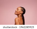 Side view of a female model having healthy and flawless skin. African american woman with braided hairstyle on pink background.