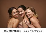 Small photo of Cheerful women standing together against brown background. Three young women with skin problems seem to look beyond their imperfections and be happy.
