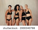 Women of all ages celebrating the beauty of aging and natural bodies. Four confident women smiling cheerfully while wearing black underwear and standing together against studio background.